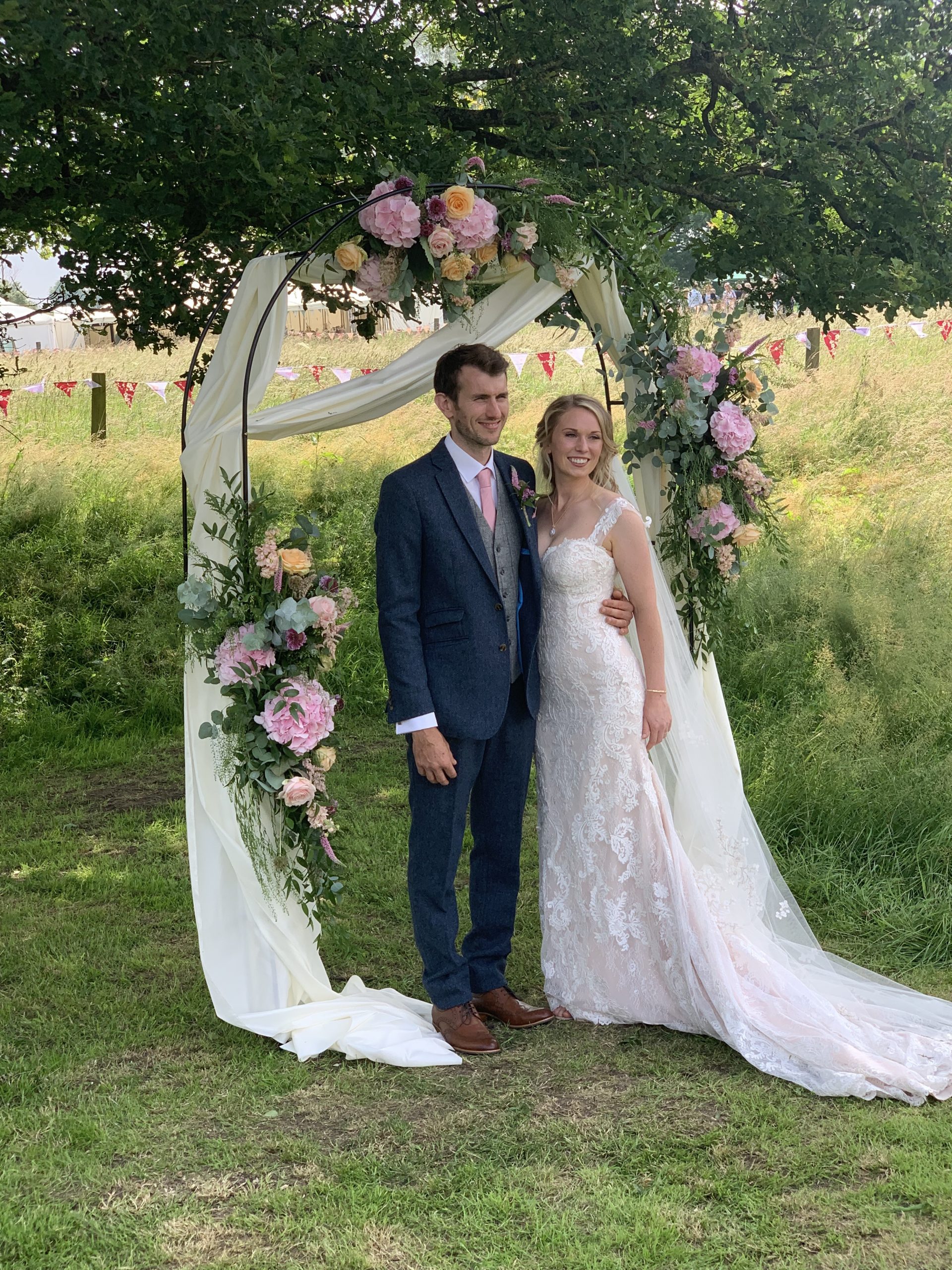 Bride and Groom standing underneath flower arch in a field