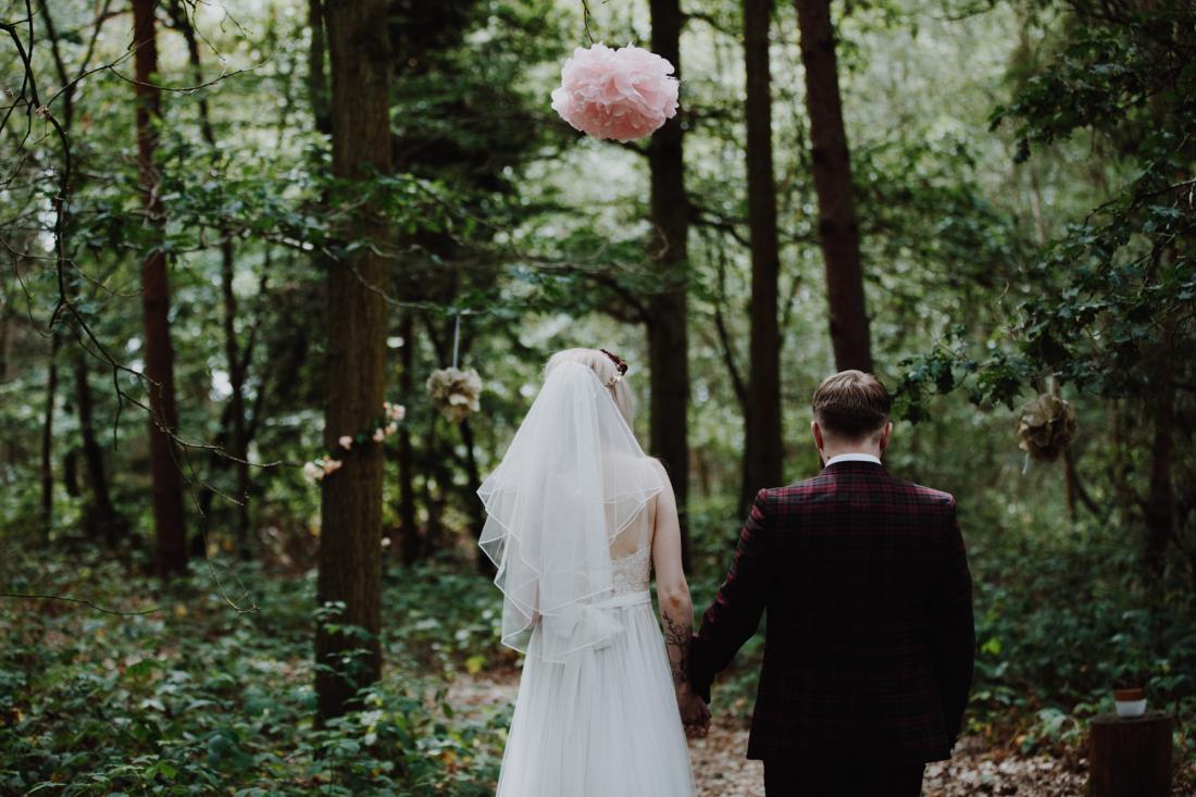 bride and groom stand with their back to the camera, surrounded by woodland for their outdoor ceremony
