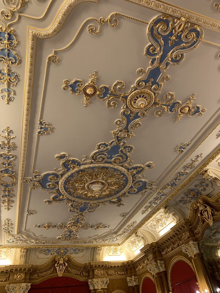 Decorative ceiling in the banqueting room of Hylands House, Essex. It is a baroque style moulding on a white background, decorated with blue and gold.