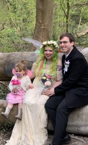 bride and daughter as flower fairies sitting on a tree trunk with groom