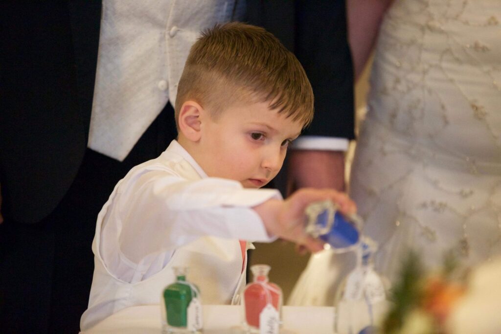 A young boy pours blue sand into a heart shaped vase as his dad and his new wife marry, to demonstrate the inclusion of children into this new family unit.