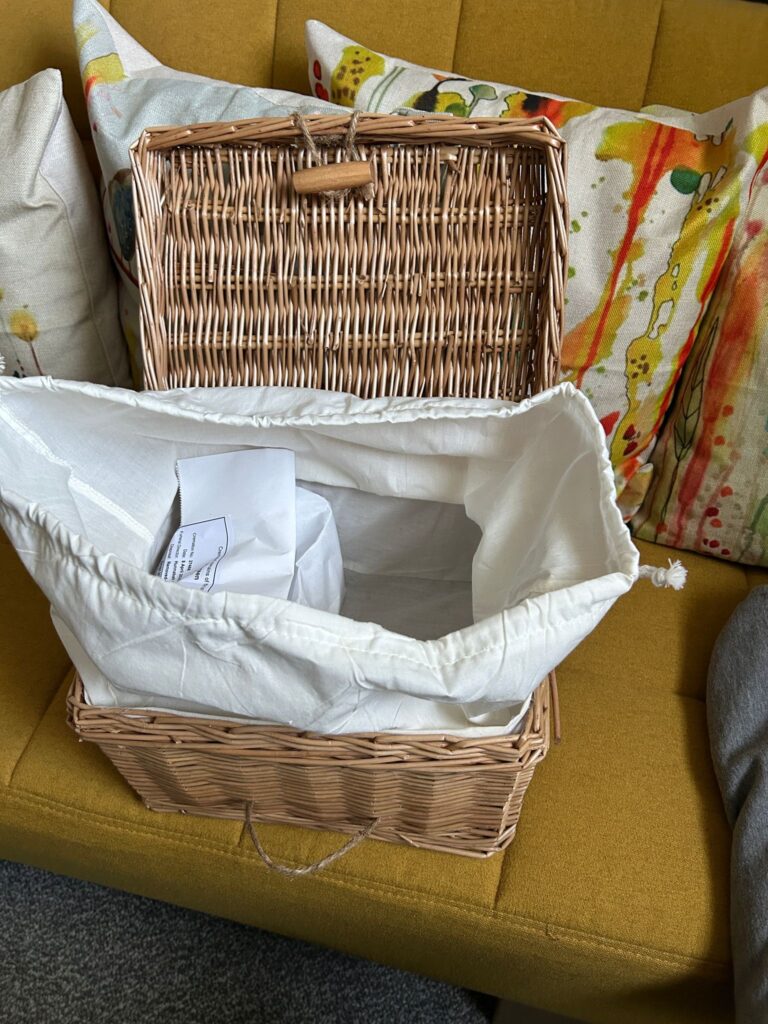 A Wicker basket sits on a yellow sofa with a package of cremation ashes inside, ready to have a second package added and be interred at a funeral.