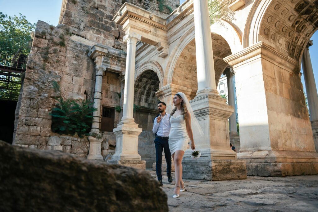 A couple walk through the ruins of a temple at twilight, the woman carries a bouquet of flowers and wears a vow indicating they have just renewed their vows.