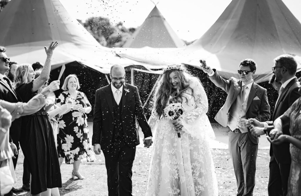 A bride and groom walk hand in hand down the ailse with tipis behind them