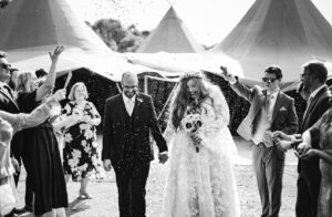 A bride and groom walk hand in hand down the ailse with tipis behind them