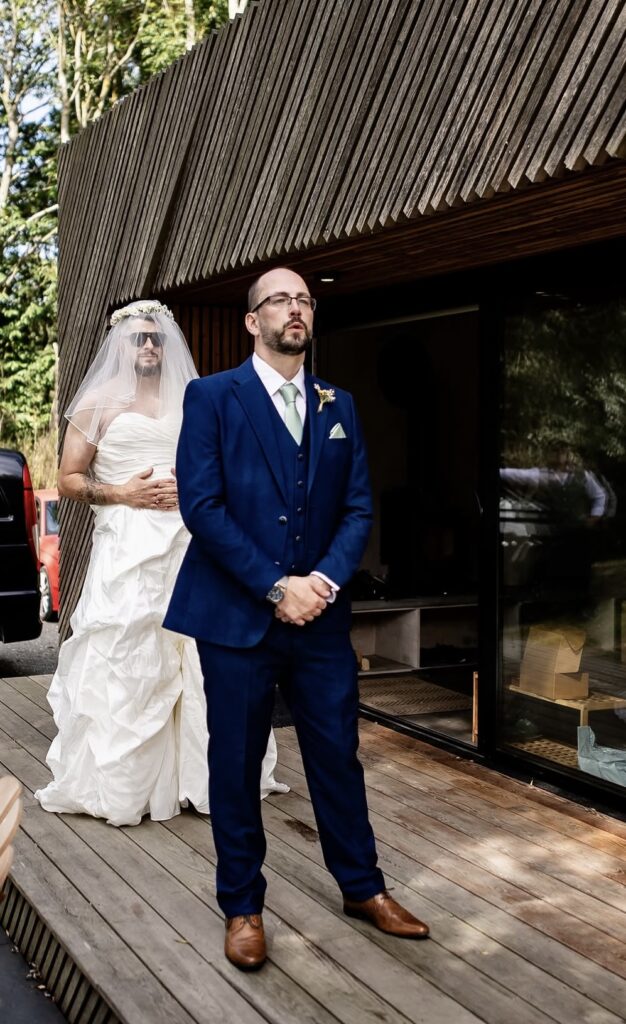 A man dressed in a bridal gown waits to surprise an expectant groom