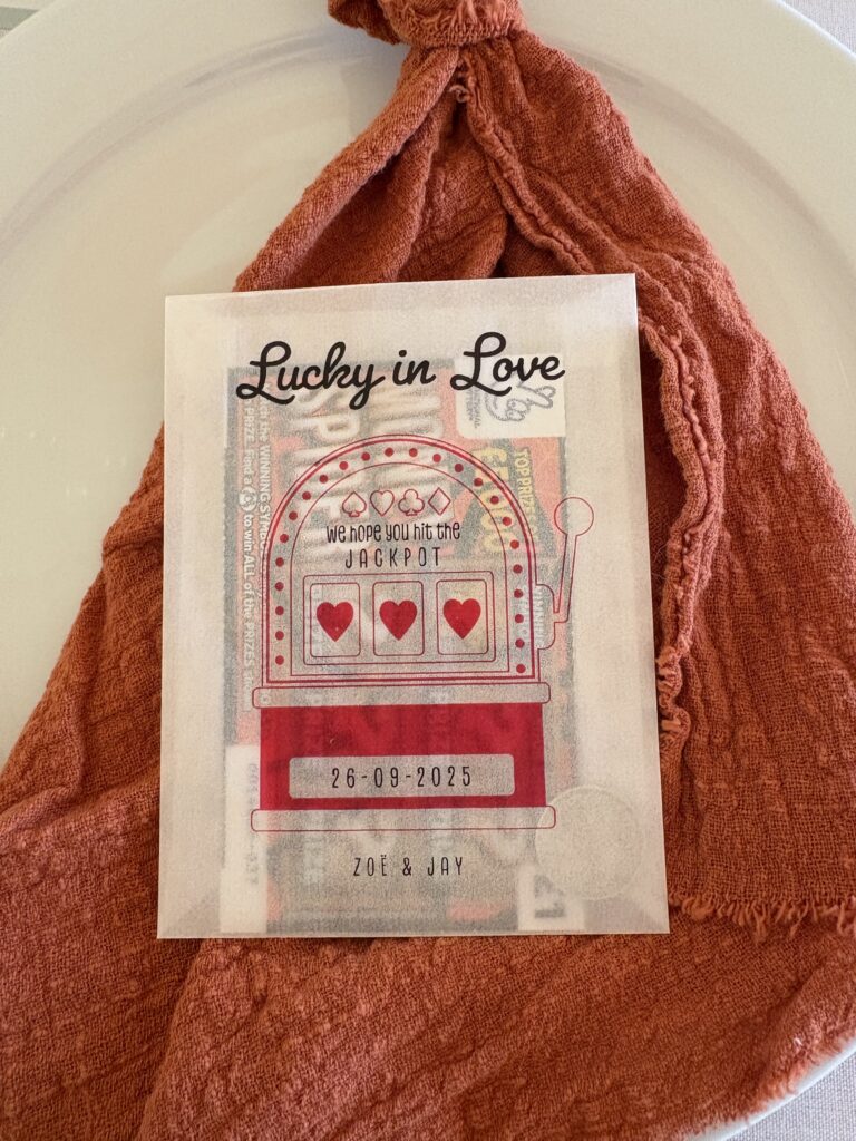 A scratch card and a coin in an envelope saying lucky in love is placed on the table setting for each guest