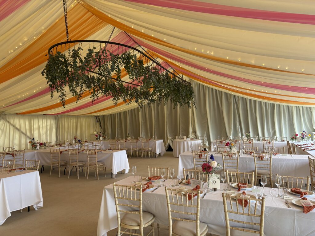A neutrally decorated marque is adorned with colourful drapes in pink and orange and matching napkins