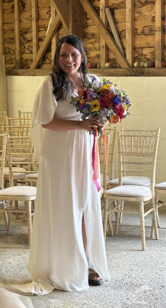 A Bride dressed in white holds a colourful bouquet in a historic barn