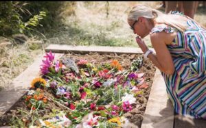 A lady blows a kiss over a flower adorned grave