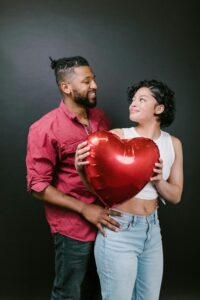A man and woman of colour look lovingly at each other over a red heart shaped balloon